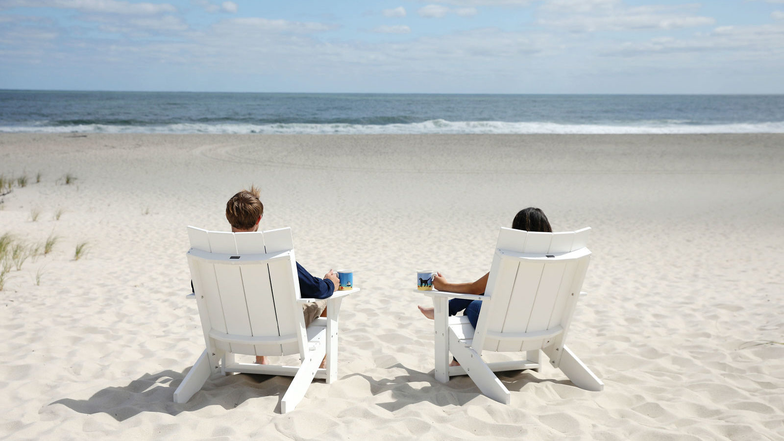 photo of two people sitting in beach chairs on a beach with beach dog mugs
